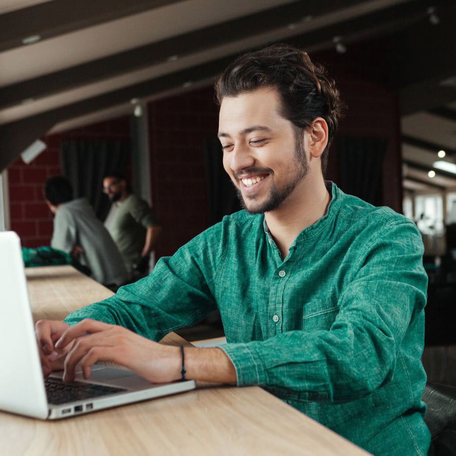 man wearing a netgain-green button down, typing on a computer at a co-working space