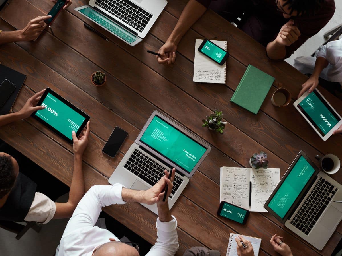 eagle-eye shot of a communal conference table with team members seated around it on various laptops and devices