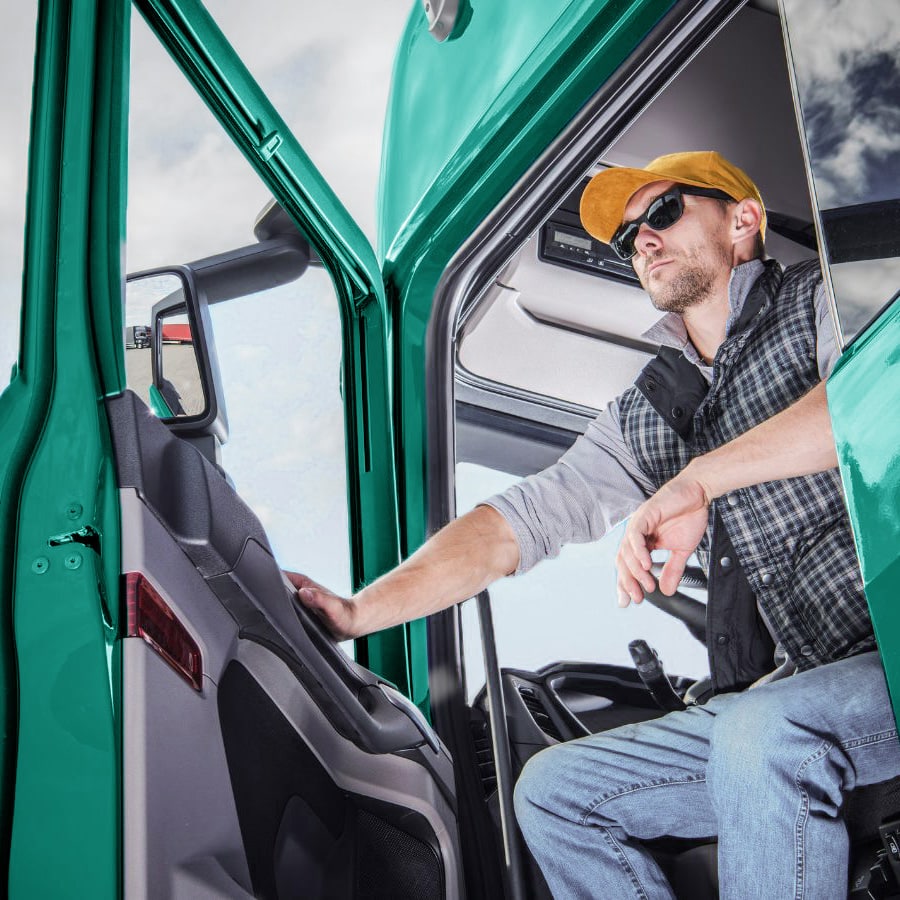 a man seated in the front seat of a netgain-green semi truck; the door is open and he is leaning out of the cab