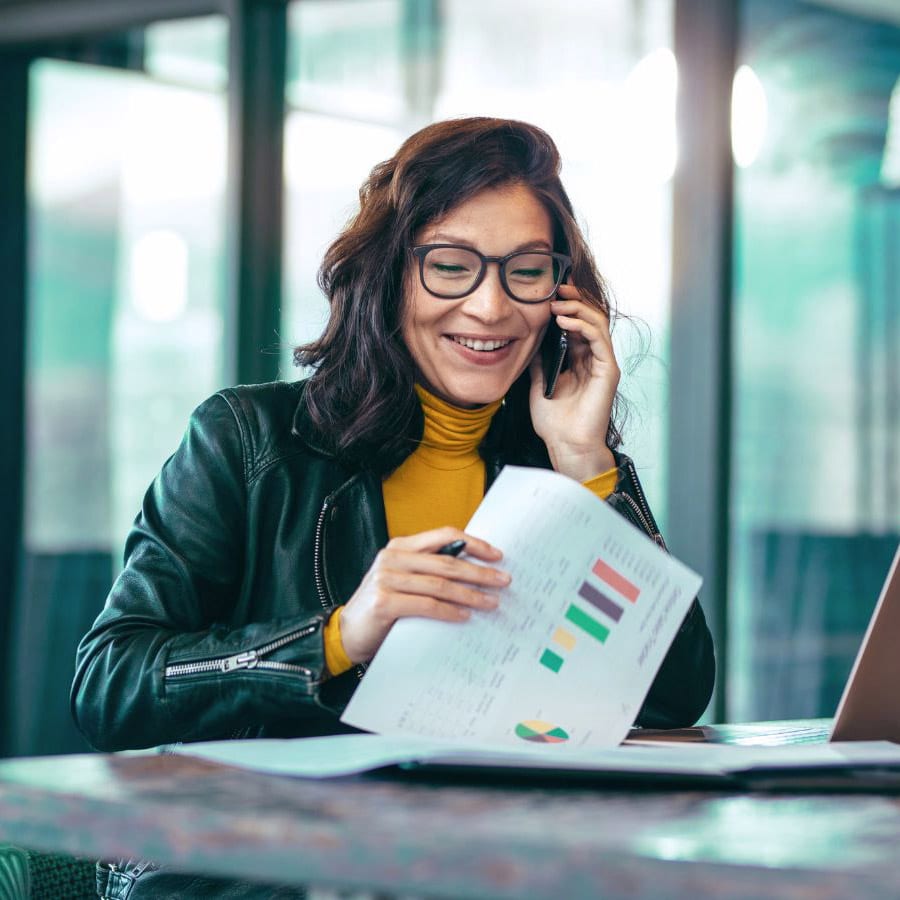 a woman smiles as she speaks on the phone, in her hand is a paper with a bar chart on it
