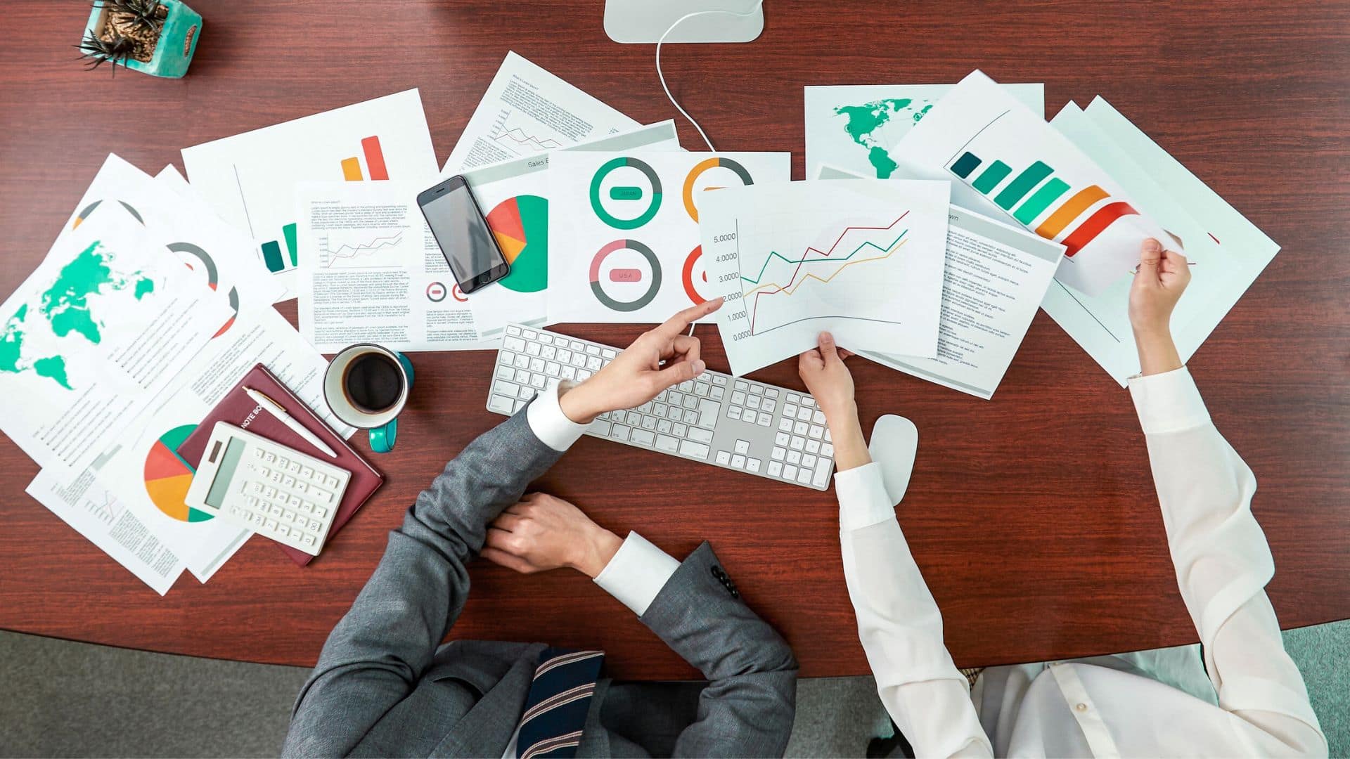 overhead shot of two people at a desk with various chart print-outs around them