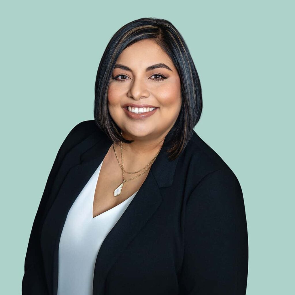 Gina Sena, woman with a white v-neck and black blazer, smiling against a seafoam green background