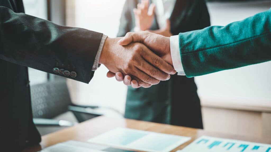 shaking hands over financial documents while someone applauds in the background