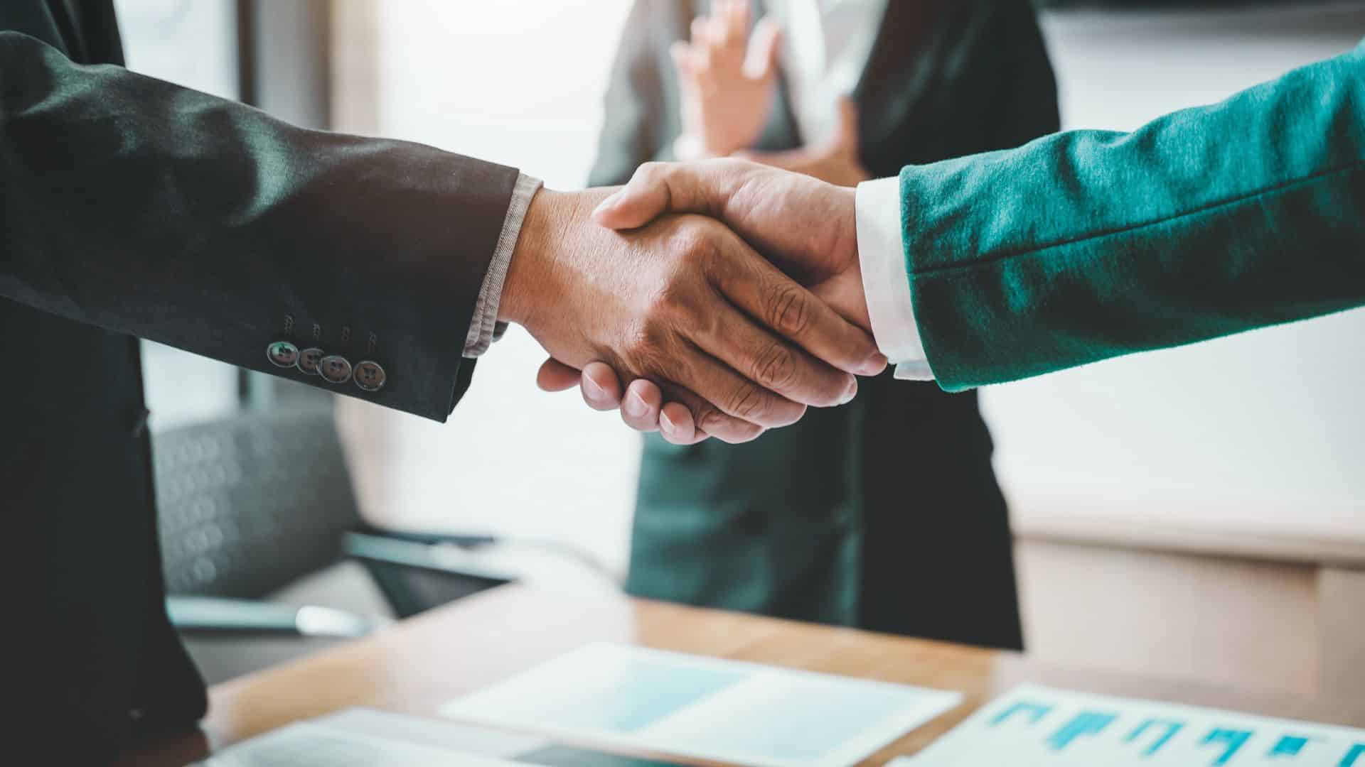 shaking hands over financial documents while someone applauds in the background