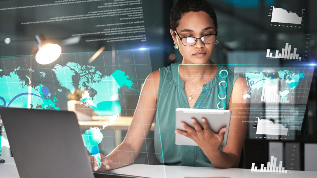 woman with a tablet in hand, sits behind a laptop, with illustrated ERP system overlay