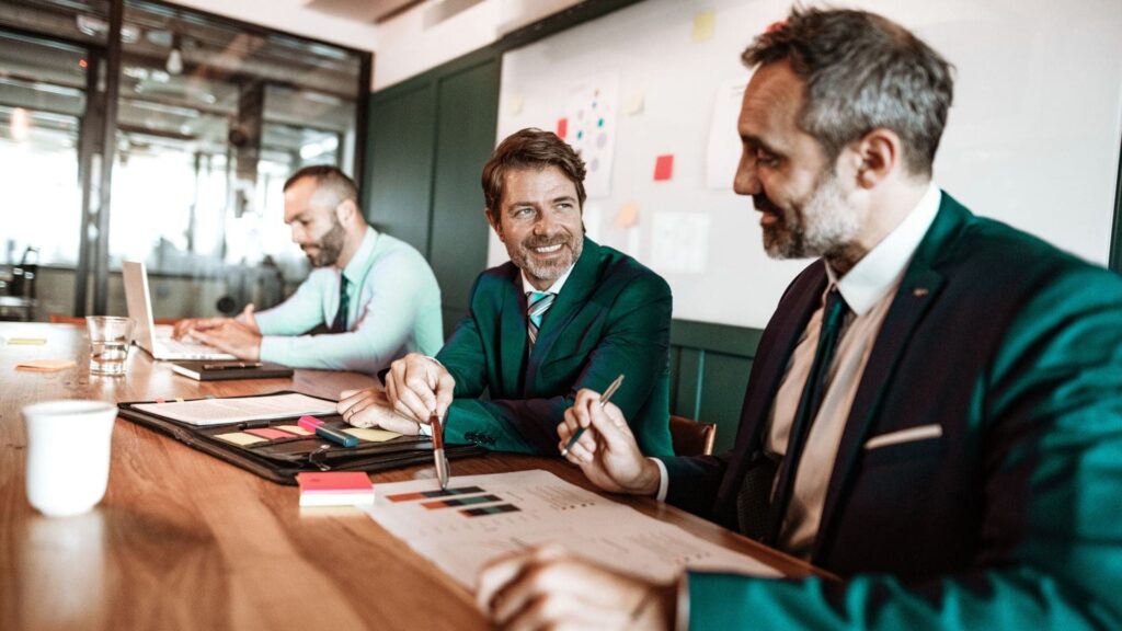 men sitting at a boardroom table smiling and talking