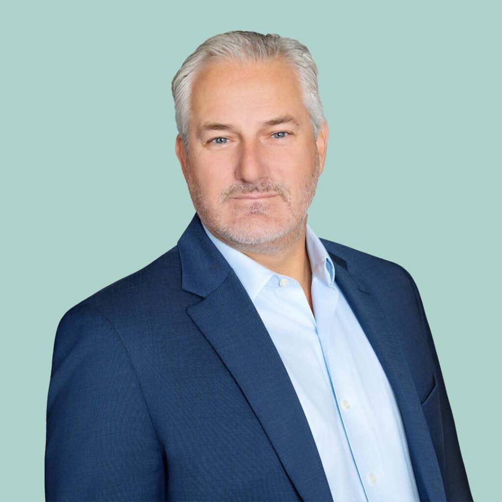 Evan Lambert; man with short gray hair and stubble wearing a dark blue blazer and light blue button-up