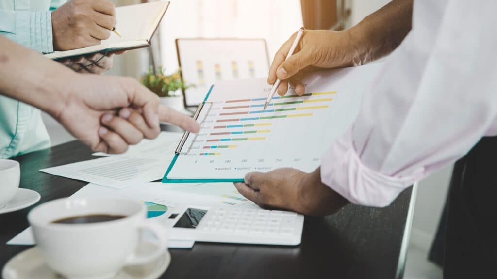 close-up of people's hands as they hold and point at a document with financial charts on it