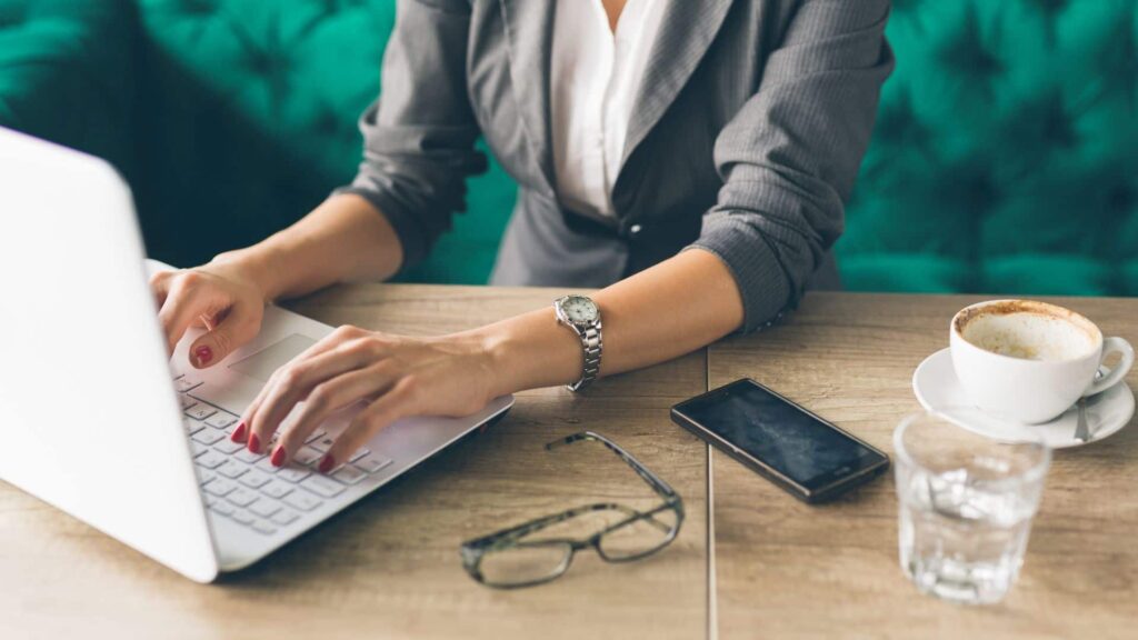 person typing on a laptop on a desk with glasses and a mobile phone next to the laptop