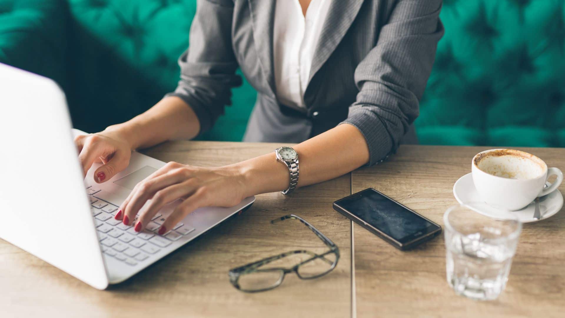 person typing on a laptop on a desk with glasses and a mobile phone next to the laptop